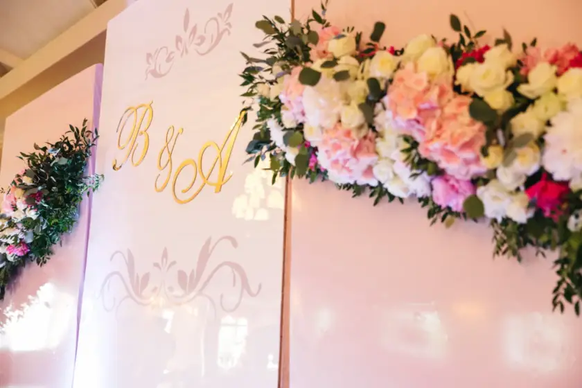 Decoración floral elegante con letras doradas "B&A" en un fondo rosa, ideal para eventos y celebraciones.