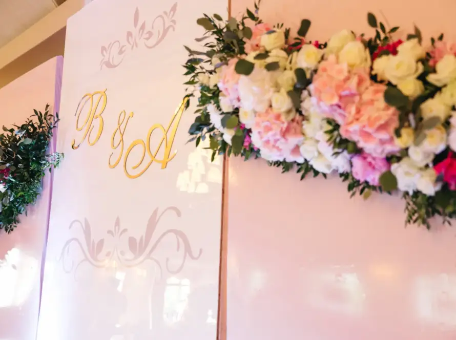 Decoración floral elegante con letras doradas "B&A" en un fondo rosa, ideal para eventos y celebraciones.