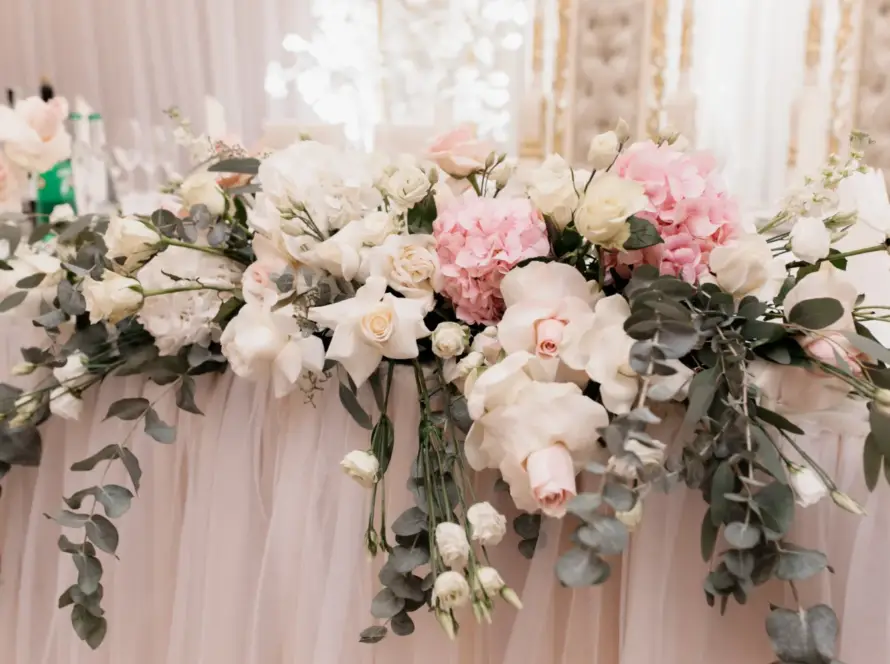Arreglos florales elegantes con rosas blancas, rosas rosadas, hortensias y hojas de eucalipto sobre una mesa decorada con tela blanca, ideales para eventos y bodas.